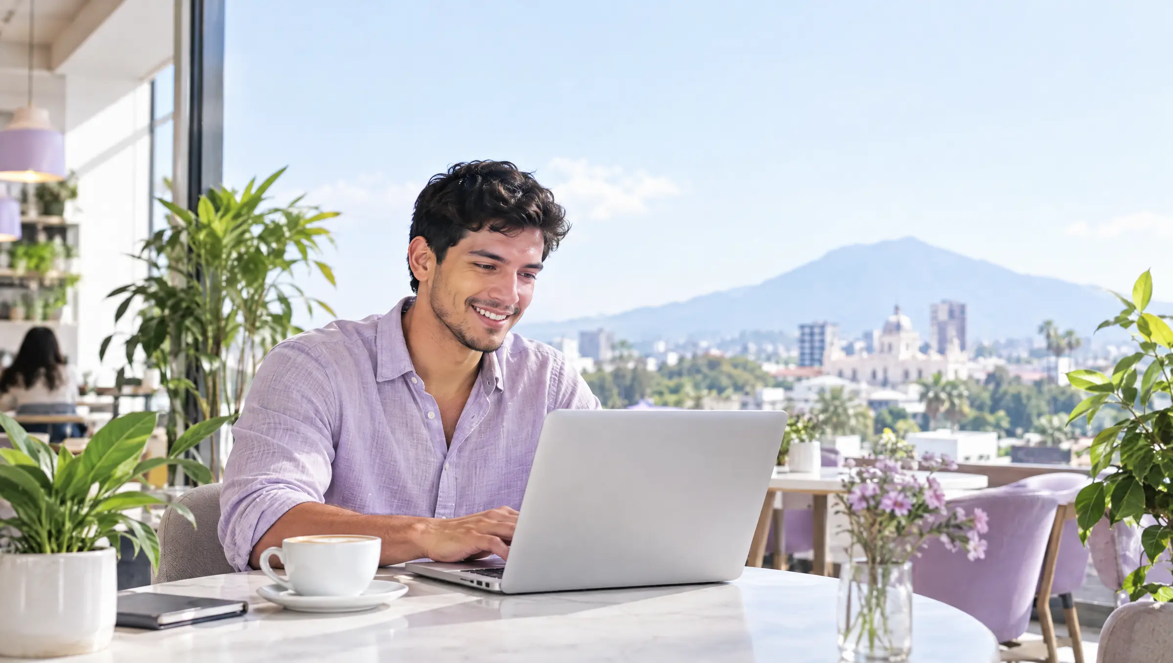 A man smiles at his laptop in a café overlooking San Salvador