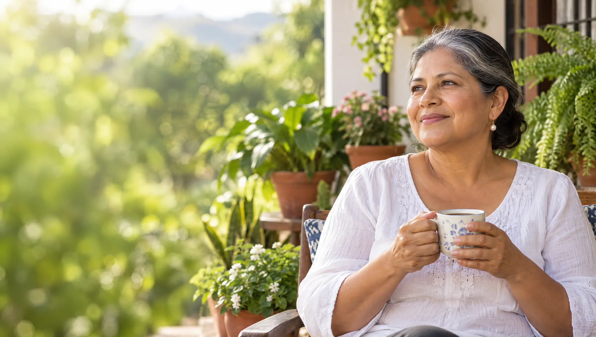 Una mujer toma café tranquila en la terraza de su casa, rodeada de plantas