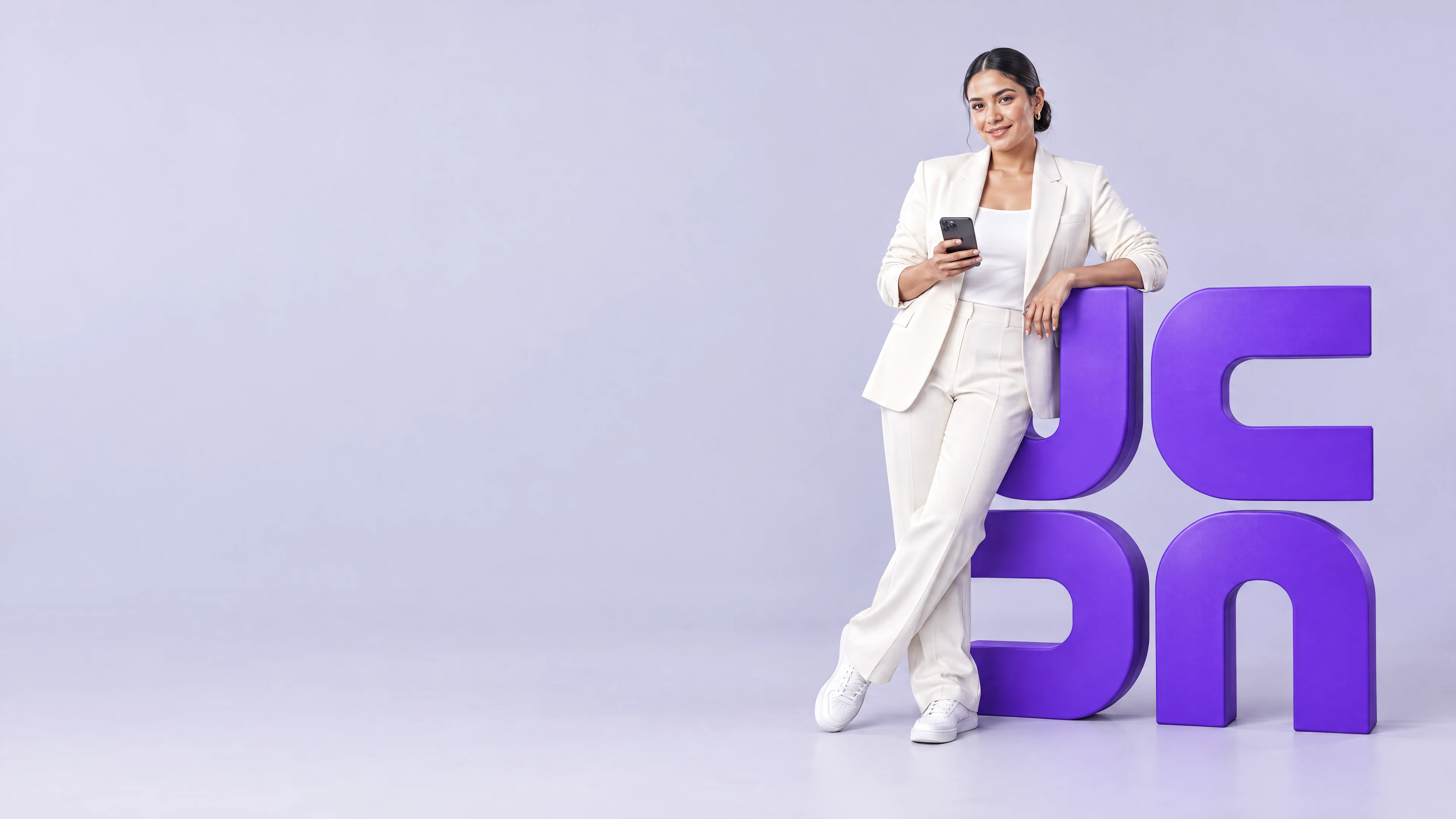 A woman in an ivory linen suit leans on a violet sculpture of the Unique Capital logo mark and looks at the camera, phone in hand, in a studio with a pale lilac backdrop